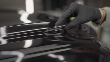 Car wrapping specialists straightening vinyl foil or film to remove ari bubbles cut carbon film. The protective film is removed from the machine with a paper knife