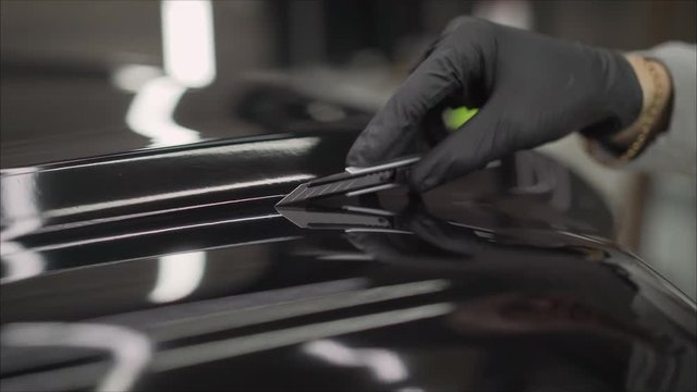 Car wrapping specialists straightening vinyl foil or film to remove ari bubbles cut carbon film. The protective film is removed from the machine with a paper knife