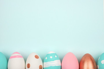 Easter bottom border of pink, white, blue and rose gold Easter Eggs against a pastel blue background. Top view with copy space.
