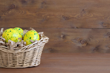 Easter yellow eggs in a straw basket. On a brown wooden background.