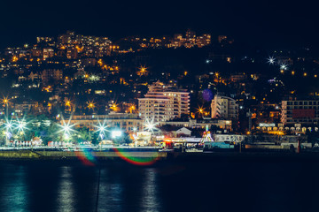 Fototapeta na wymiar Yalta embankment at night, city buildings lights reflected in black sea, beautiful resort in Crimea with mountains and sea