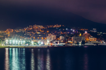 Obraz premium Yalta embankment at night, city buildings lights reflected in black water, beautiful resort in Crimea with mountains and sea