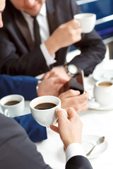 Coffee break. Vertical cropped closeup of a businessman holding a cup of coffee at a meeting in a restaurant selective focus on a cup