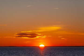 bright orange sun with reflection in the water during sunset over the sea