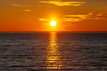 bright orange sun with reflection in the water during sunset over the sea