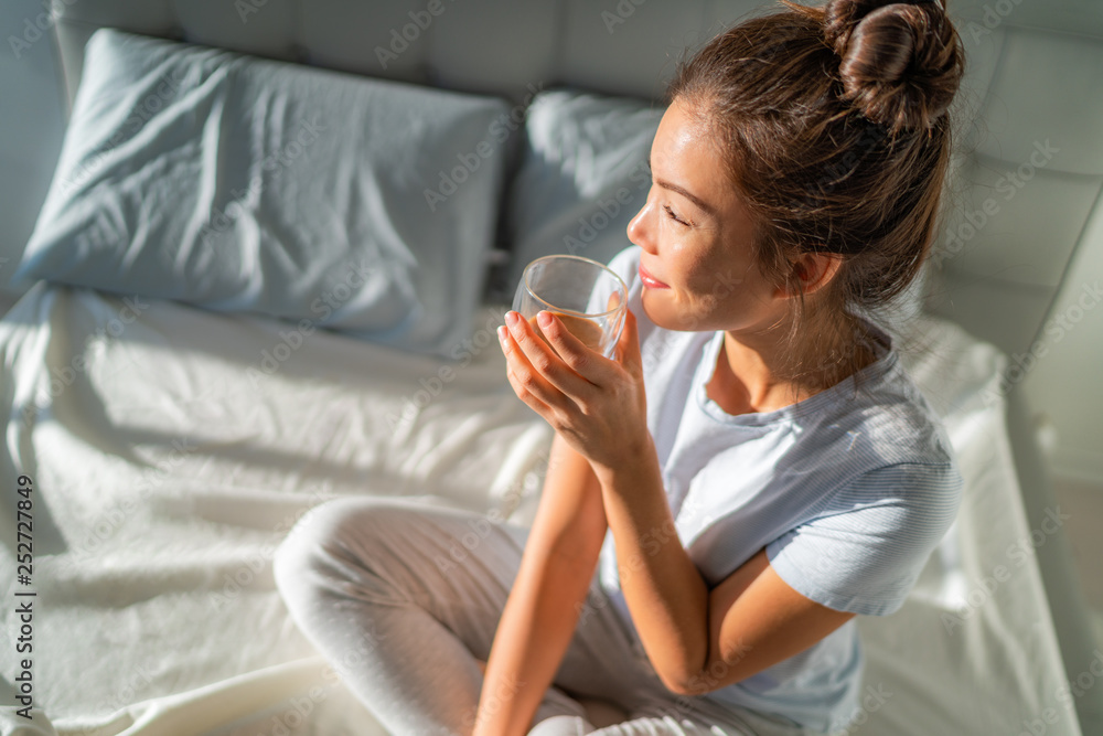 Wall mural morning breakfast in bed happy asian woman drinking hot coffee mug relaxing sitting on mattress. wee