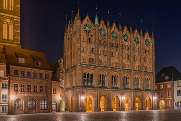 Stralsund – Rathaus mit Schaufassade, dahinter die Nikolaikirche am Alten Markt bei Nacht - obrazy, fototapety, plakaty