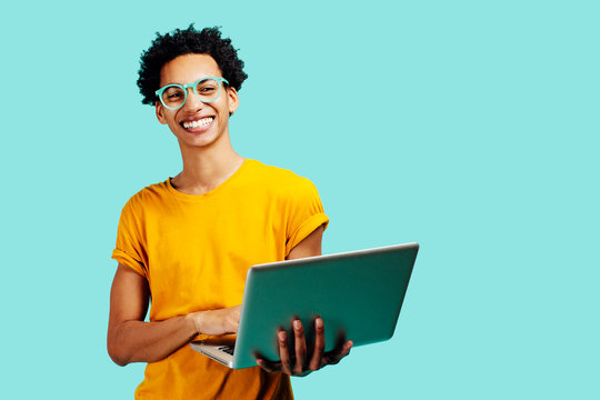 Portrait of a smiling young man with glasses holding his laptop, isolated on blue background