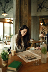 Young woman relaxing in a cafe while reading newspaper during her coffee time.