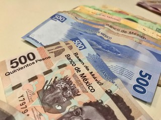 Many mixed Mexican peso bills spread over a beige desk