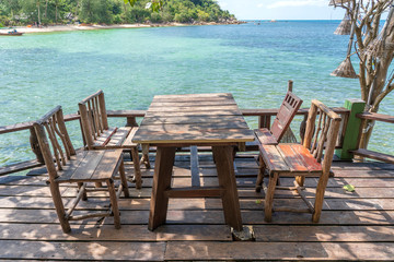 Wooden table and chairs in empty beach cafe next to sea water. Island Koh Phangan, Thailand