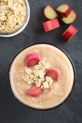 Vegan rhubarb and oatmeal smoothie in glass, garnished with oats and cooked rhubarb pieces, photographed overhead on slate (Selective Focus, Focus on the top of the smoothie)