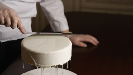 Obraz na płótnie Canvas Confectioner fills cakes with white liquid glaze. She equals top surface of cake.