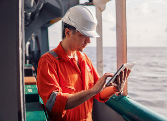 Marine chief officer or captain on deck of vessel or ship watching digital tablet. Internet and...