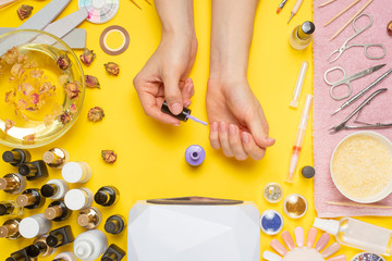 Manicure - means for creating, gel polishes, all for nail care, beauty concept, care. On a yellow background, a woman receives a manicure of nails. Service set