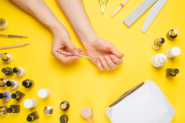 Manicure - tools for creating, gel polishes, all for nail care, beauty concept, care. On a yellow background, a woman gets a manicure of nails.