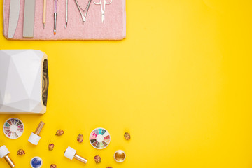 A set of cosmetic tools for manicure and pedicure on a purple background. Gel polishes, nail files and nippers and a top view of the lamp. Flat lay. on yellow background