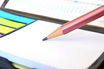 Tip of the sharp pencil writes on a white sheet of paper for notes on the background of the calendar and colored stickers. Close up