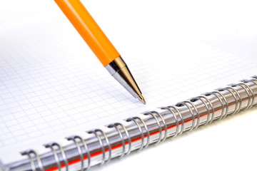 Tip of the yellow ballpoint pen writes on a empty white sheet of notebook. Close up