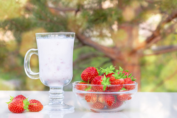 Fresh ripe strawberries in a bowl and iogurt on a white table outdoors on a summer day