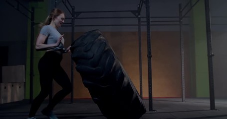 Caucasian female athlete flipping large tire in a gym. Cross workout training. 4K UHD