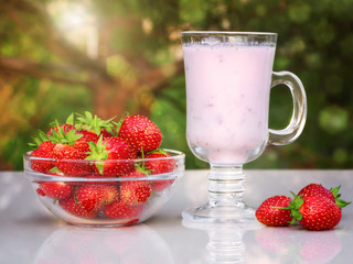 Fresh ripe strawberries in a bowl and iogurt on a white table outdoors on a summer day