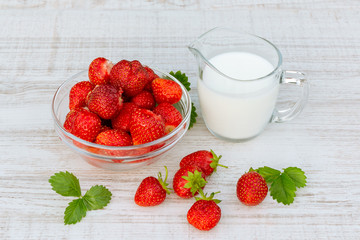 Fresh ripe strawberries in a bowl and iogurt on a white table outdoors on a summer day