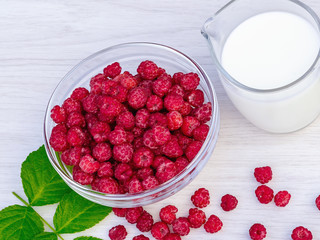 Fresh raspberries in a glass bowl and natural iogurt on a white wooden table. Healthy eating concept