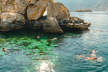 People swim with masks in the clear turquoise water of the Gulf of Oman