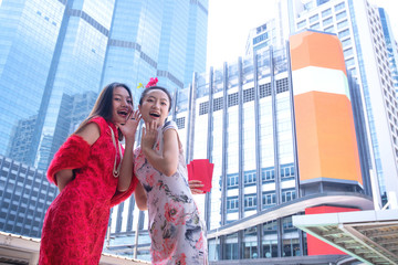 Young beautiful Asian women wearing Chinese dress traveling in city, having fun,  Ang Pao red envelopes in hand, Chinese new year concept