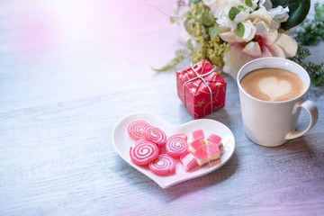 Sweet jelly in heart shaped plate for valentine's day with candle, silver star and a cup of latte coffee, gift box on wood background