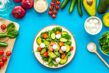Ingredients for fresh salad. Vegetables, greens, spices, plate of salad on blue background top view
