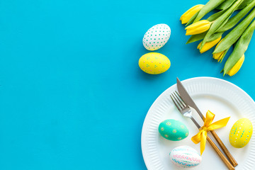 Festive traditional Easter dinner concept. Tableware, painted eggs, tulips flowers on blue table top view space for text