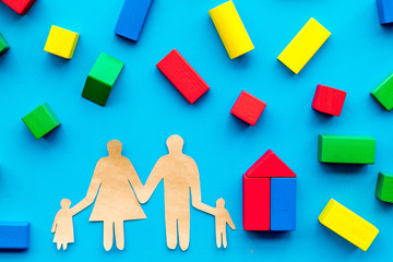 House building concept. Family cutout among colorful toy bricks on blue background top view