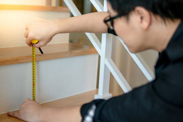 Young Asian worker using tape measure for measuring riser and thread on stair in the house. Housing...