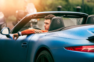 Fototapeta na wymiar Succesful young adult handsome man drives luxury convirteble sport car at sunny day