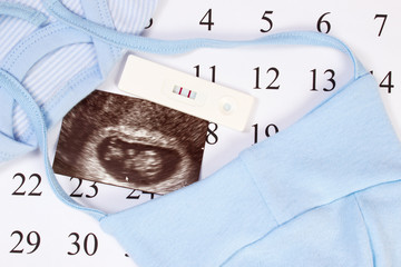 Pregnancy test, ultrasound scan of baby and clothing for newborn on calendar