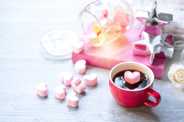 Obraz na płótnie Canvas Hot coffee with heart pink marshmallows for valentine's day, with candle, silver star, pink book and white fur on wood background
