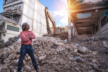 Demolition control supervisor or engineer crossed arms on the pile of bricks over large jackhammer vehicle machine