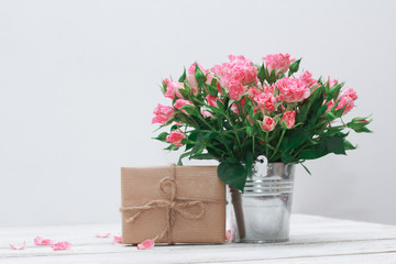 Bunch of roses in tin bucket, petals and gift box on white wooden table. Women day concept. Rough string, craft wrap, vintage, 8 march, birthday, anniversary, spring