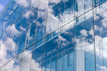 clouds reflected on glass facade wall of modern office building
