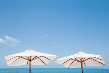white vintage umbrellas on the sand beach with beautiful blue background of the summer sky.