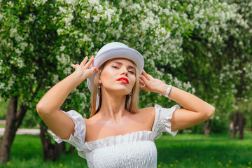 Sexy modern bride in white cylinder hat enjoing bloomin apple tree flowers.