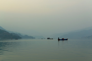 Soft image of relaxing tourists in boats on Lake Fewa in Pokhara, Nepal at sunset. Heavy smog and fog produce persistent grey conditions, creating beautiful and mysterious scenery.