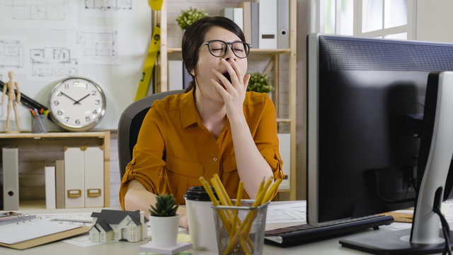 sleepy tired overworked hardworking assistant architect yawning with close eyes cover mouth want to sleep. stressed female interior designer in workplace station having computer laptop on the table.