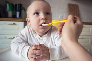 Mother feeds her little son porridge from a yellow spoon