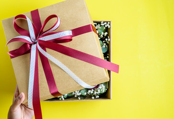 Fototapeta premium Hand open gift box with bow on yellow background