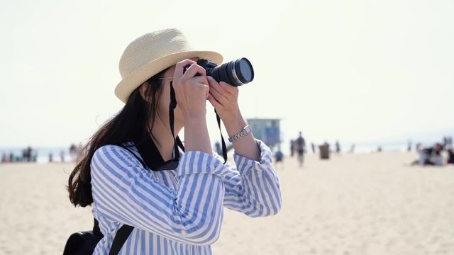 asian woman tourist photographer taking picture by professional slr camera of skylines in santa monica pier. Female traveler looking view photographing snapshots on beach. lady in hat and sunglasses