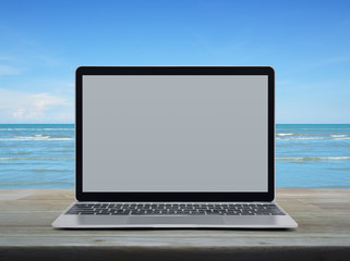 Modern laptop computer with blank grey screen on wooden table over tropical sea and blue sky with white clouds