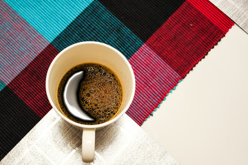 White coffee cup with moon shape reflection on white table with colorful table cloth